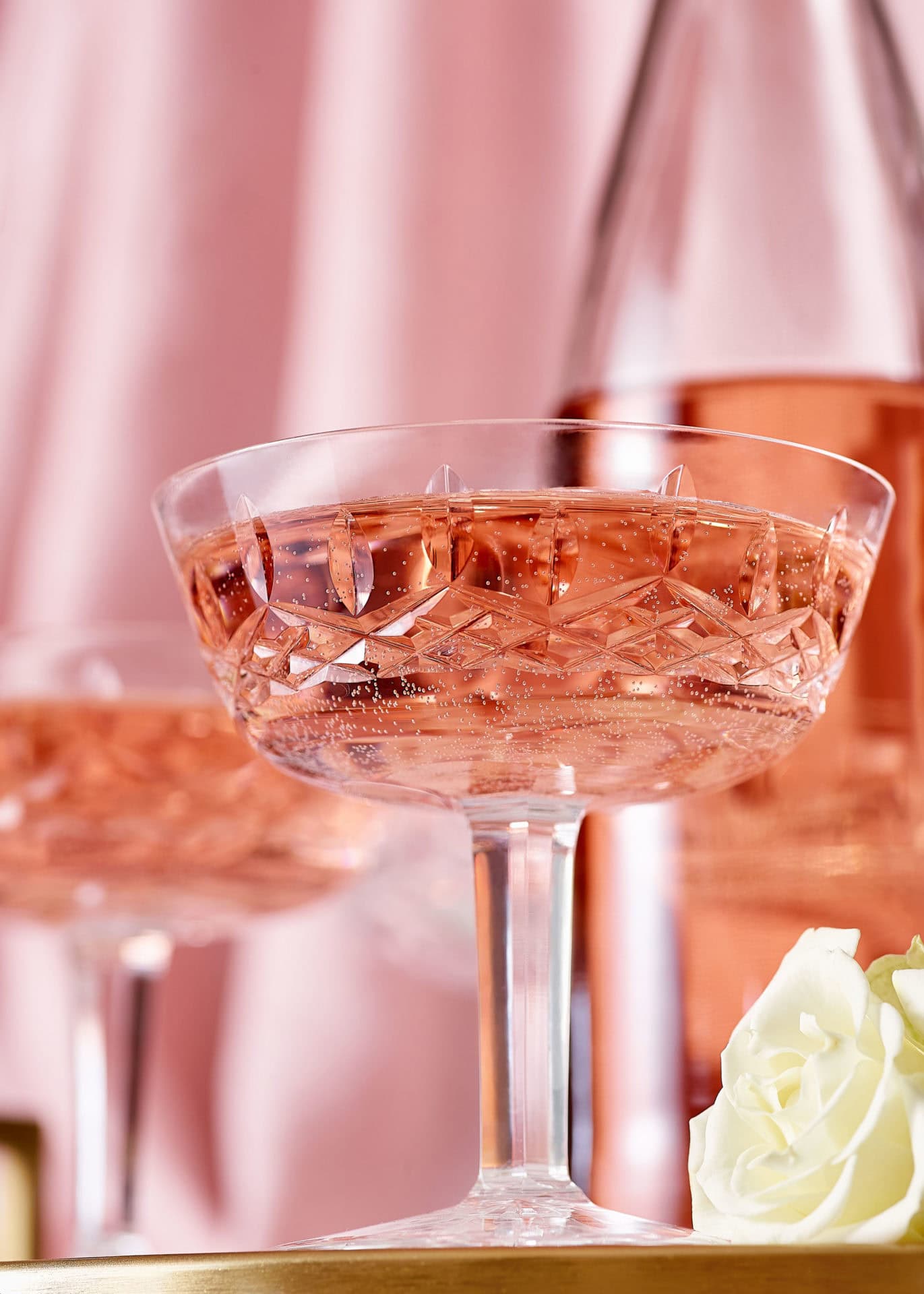 pink champagne drink in crystal glasses with pink satin background and white rose on table
