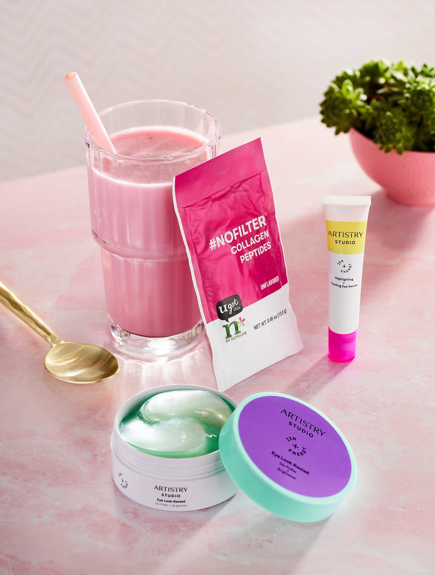 pink powder drink packet with glass of pink smoothie along with tube of cream and canister on pink table