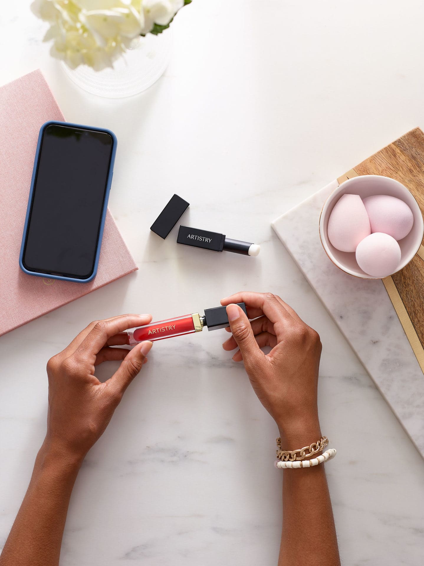 hands of woman opening lip gloss container over table.  Open lipstick on table