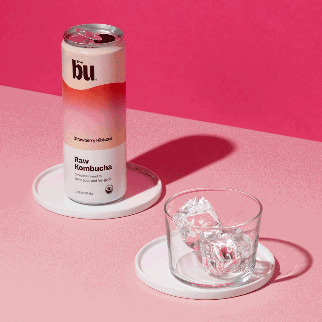 can of pink and white kombucha and glass with only ice in it on pink table with pink background