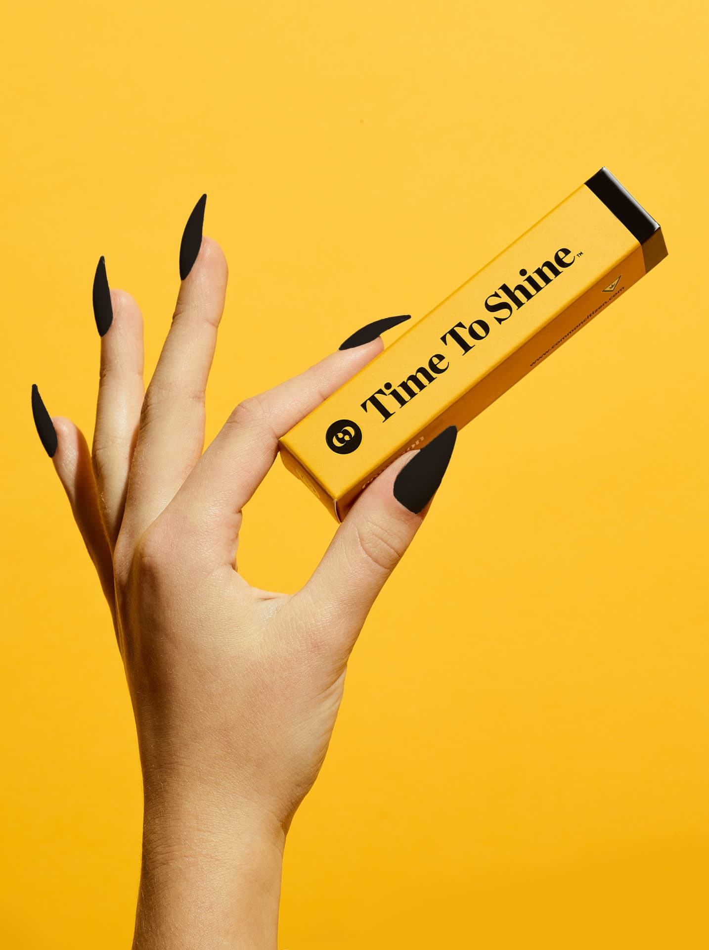 womans hand with black pointy finger nails holding a yellow rectangle box that says "Time To Shine" with yellow backdrop