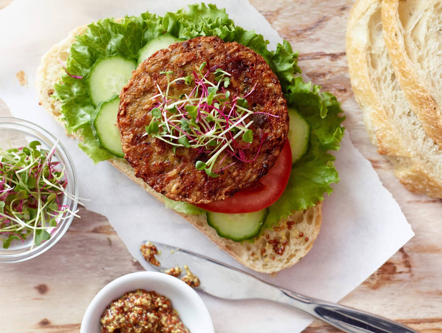 burger patty on open faced sandwhich with lettuce, cucumber and bean sprouts, ingredients also on table next to the plated sandwich