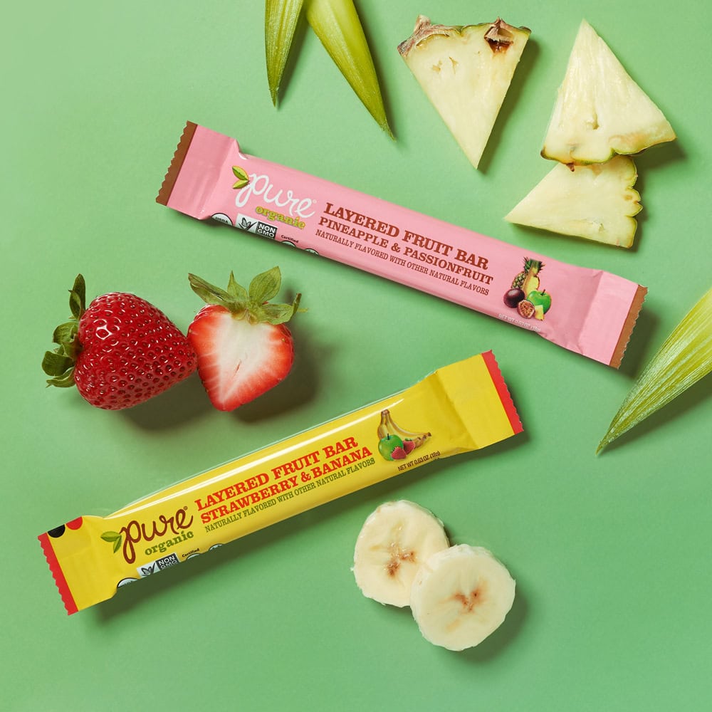 pure bar in yellow and pink packaging on green background with cut pineapple, strawberries and bananas 