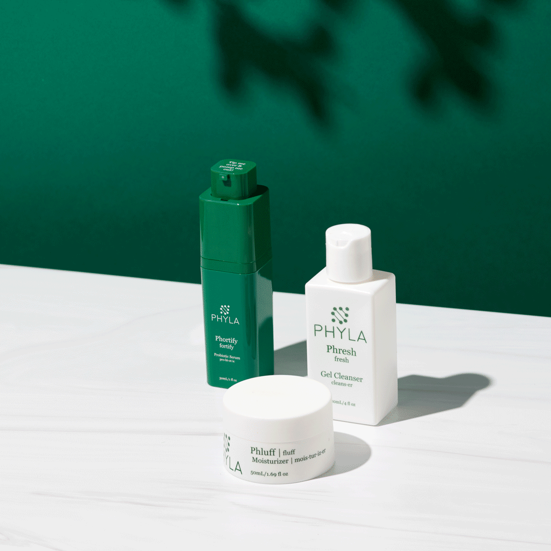 gif of woman getting a pump of Phyla lotion product on table with 2 other bottles of lotion, green background