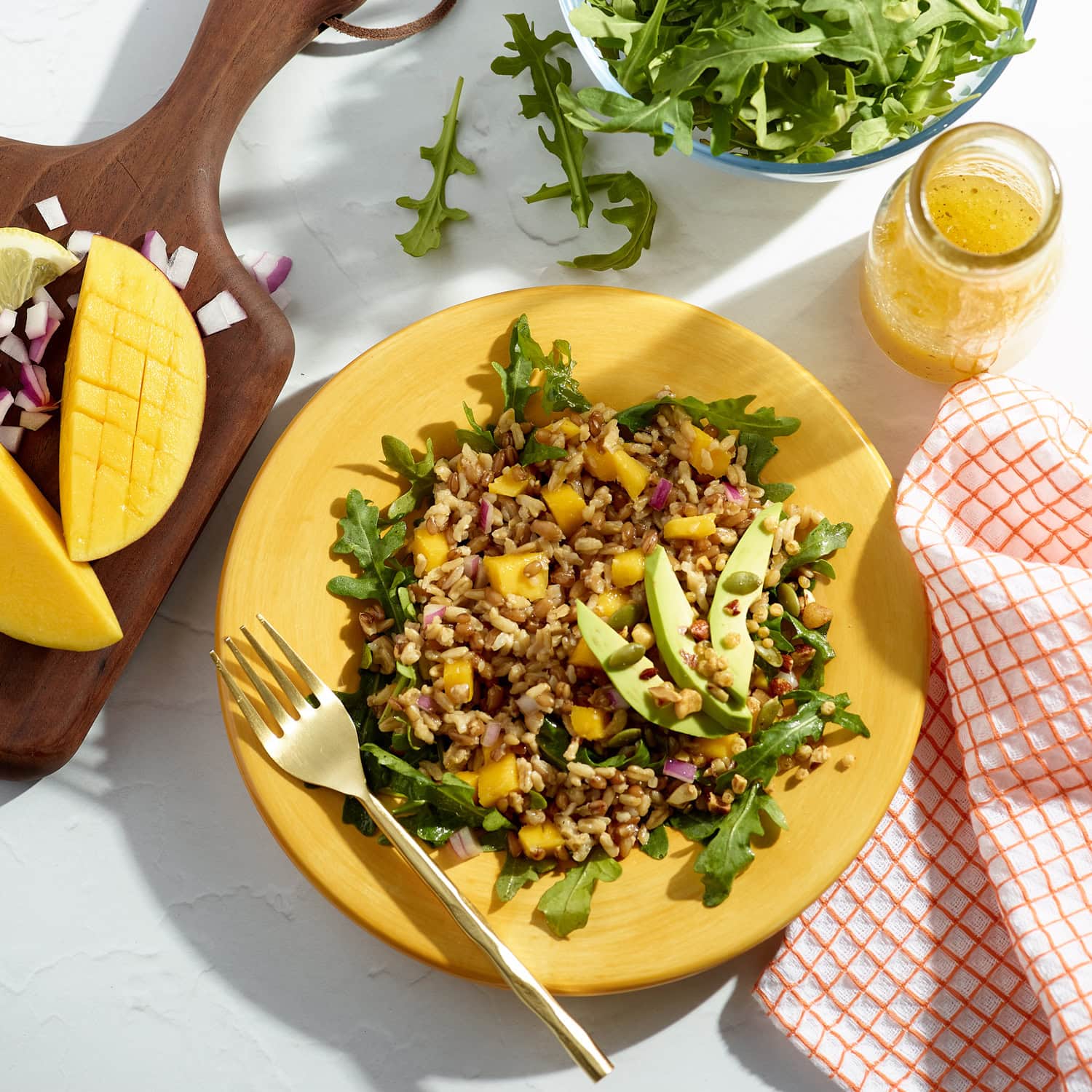 plate of rice and grains with avocado, mango, on a bed of greens with gold fork on yellow plate.   