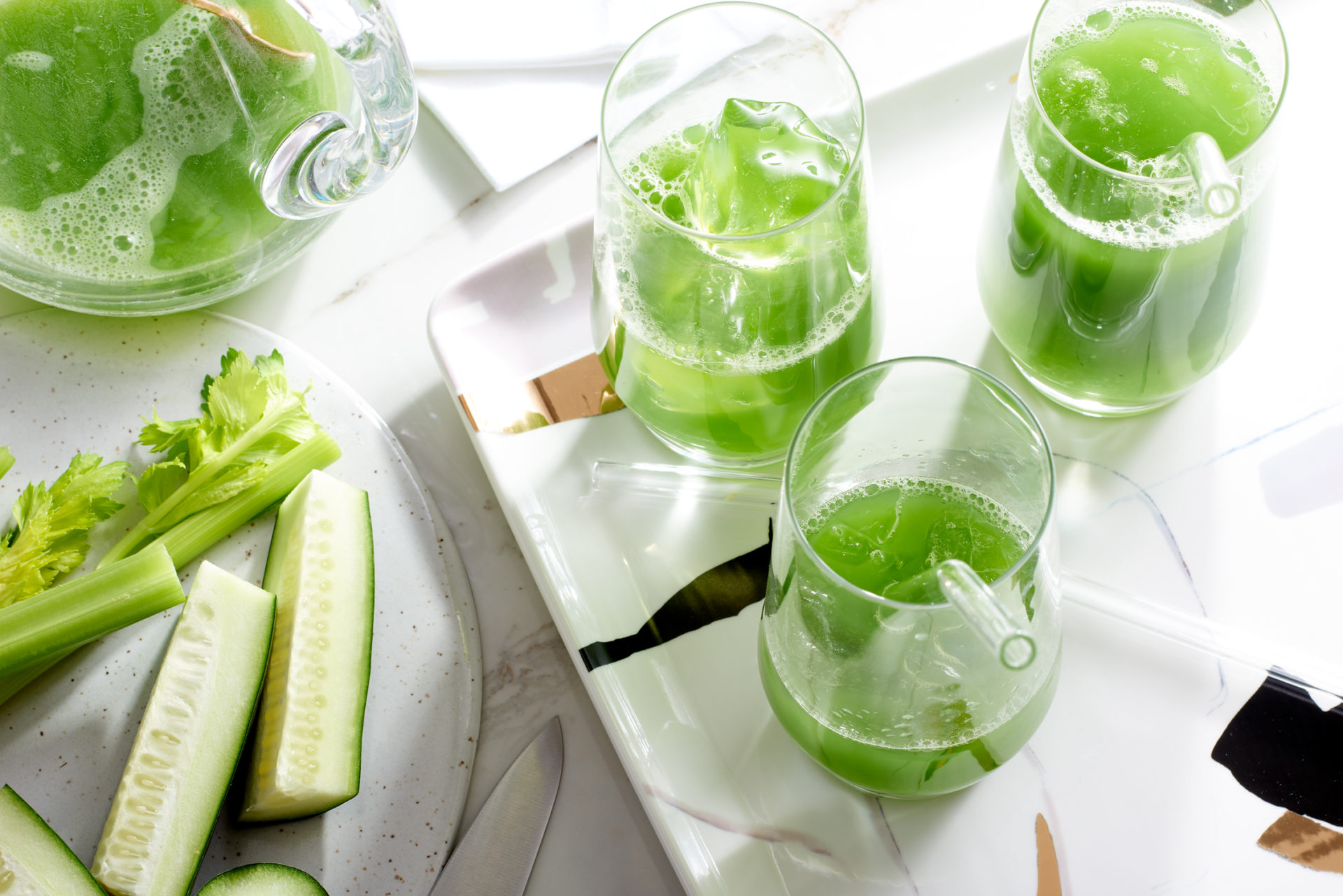 green juice drinks - 3 on a plate with ice on a table with celery and cucumber 