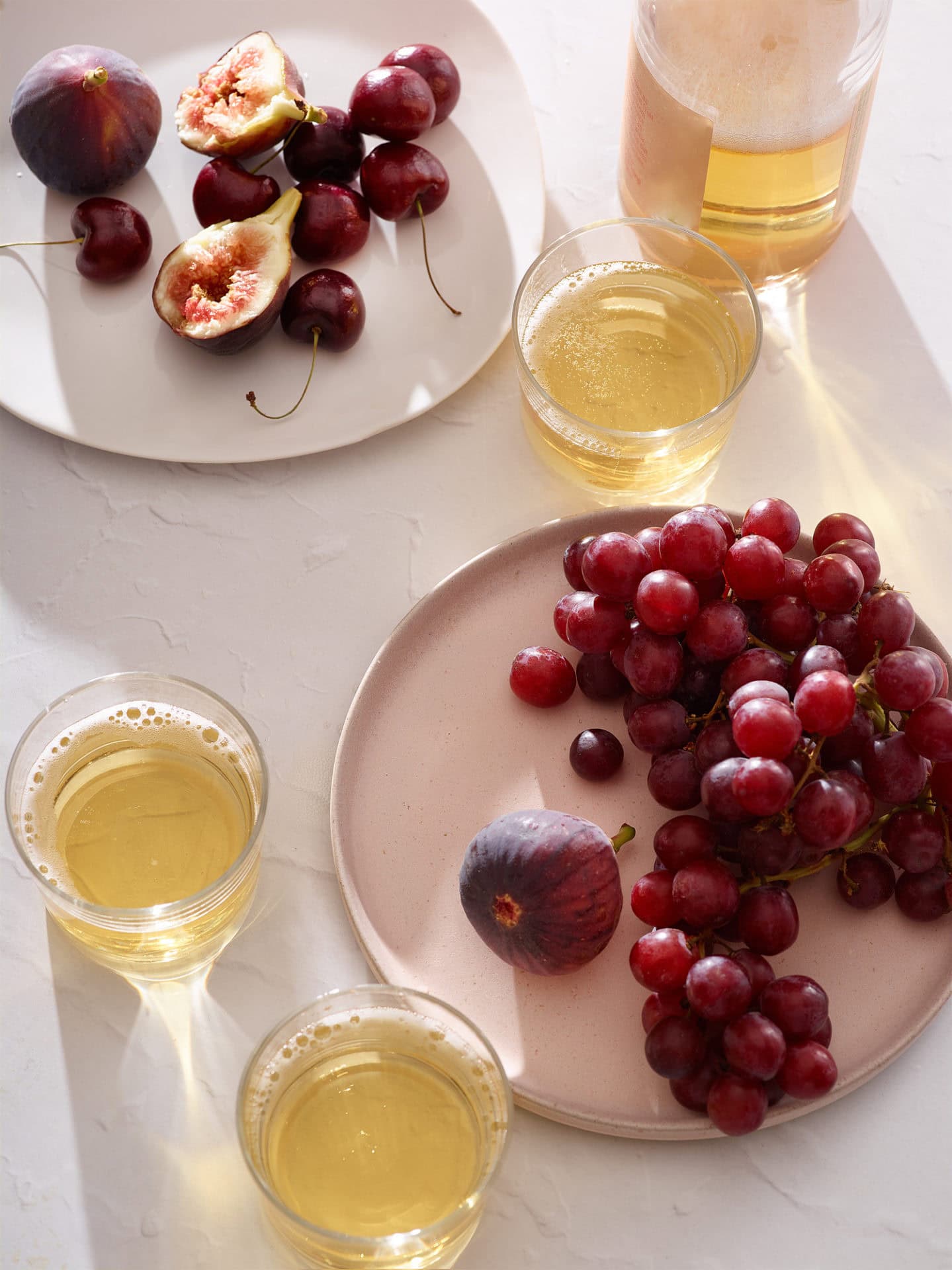 plates of fruit, grapes, figs, etc. on a table with glasses of wine and cider