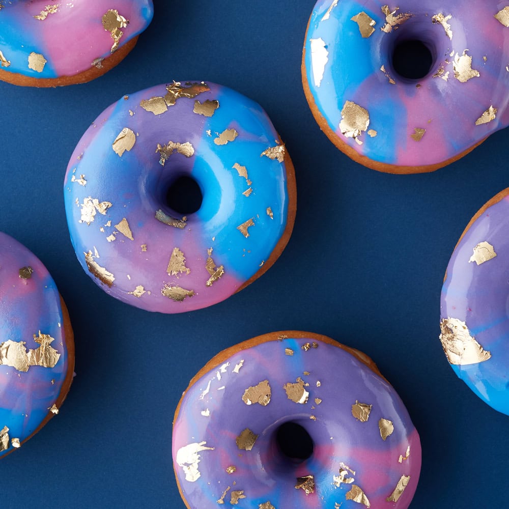 pretty glazed donuts blue, pink and purple mixed colors with gold leaf decorations laid out on a blue background