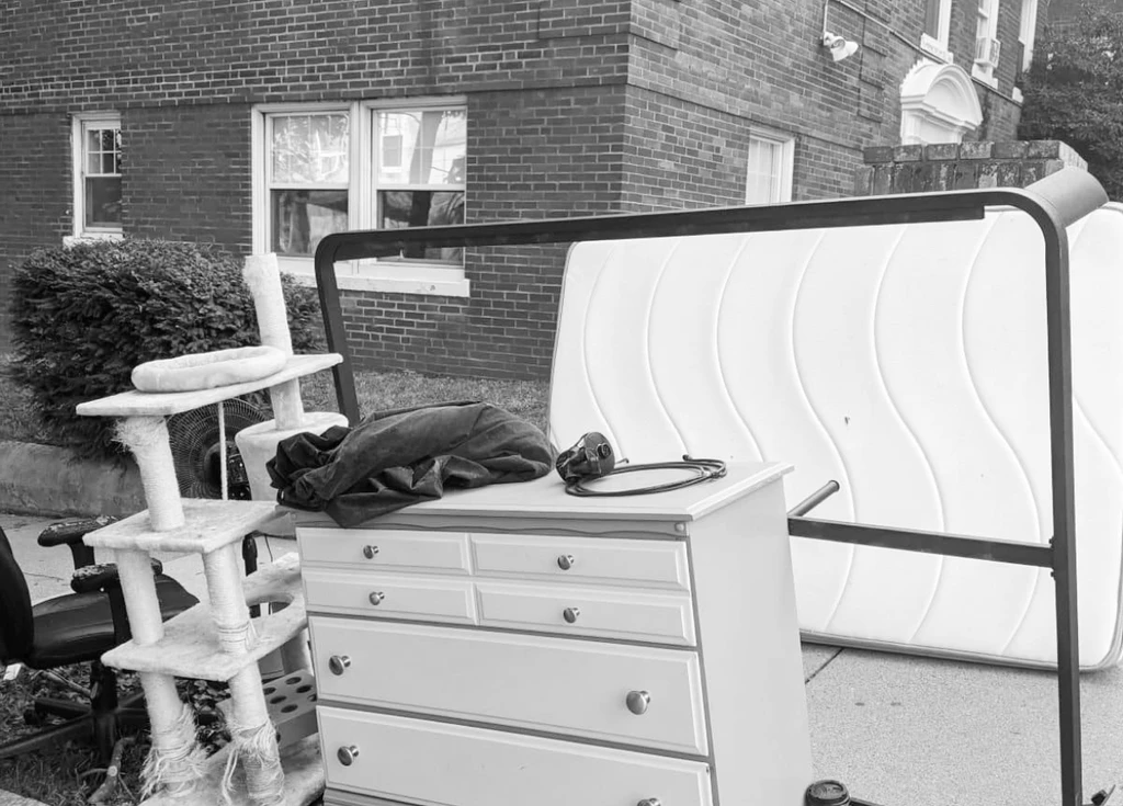 A dresser, mattress, cat tree, and office chair stacked on a residential curb