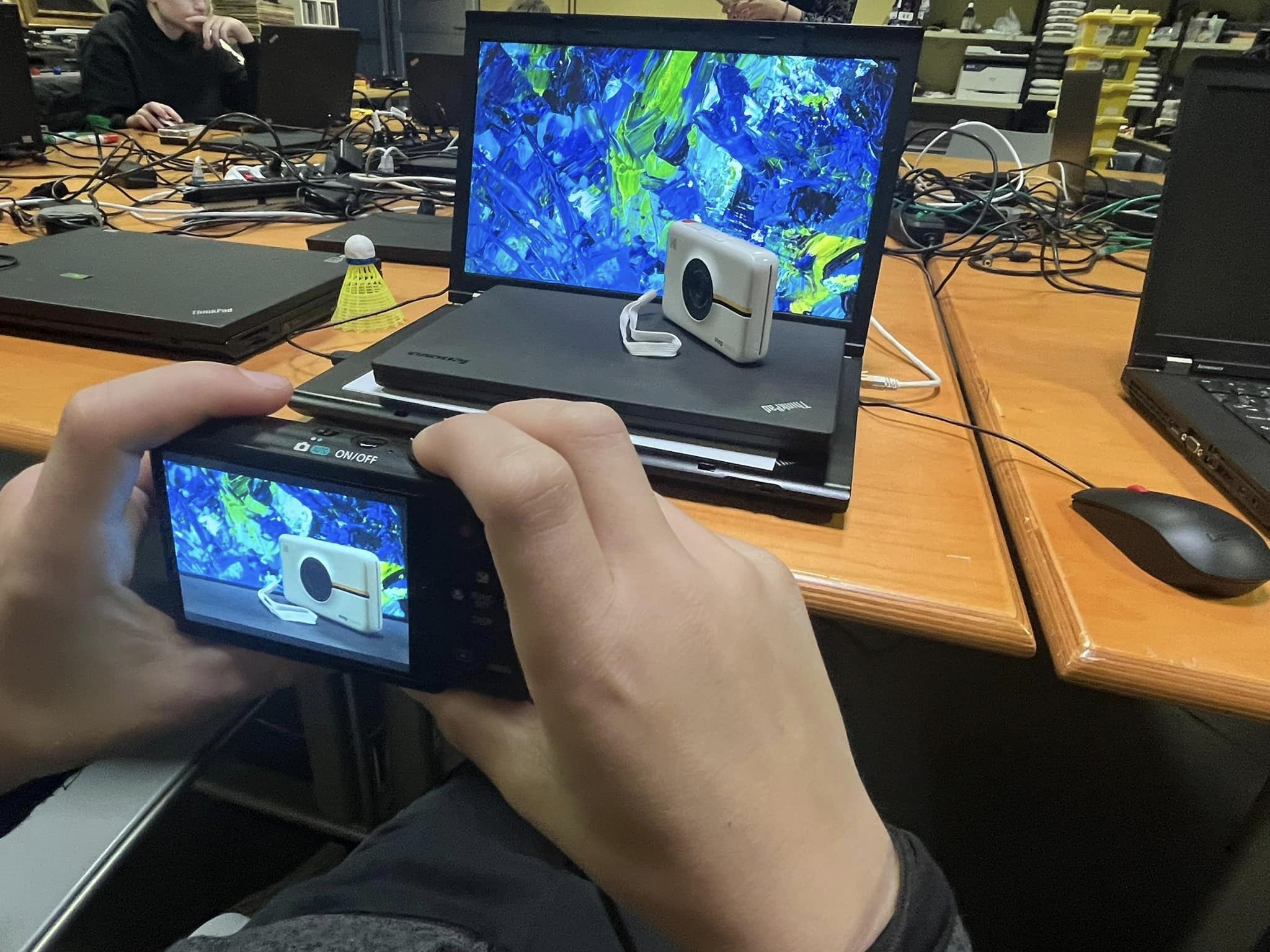 A pupil is taking a photo of a plasic model of a boat, and using laptop screen as a background