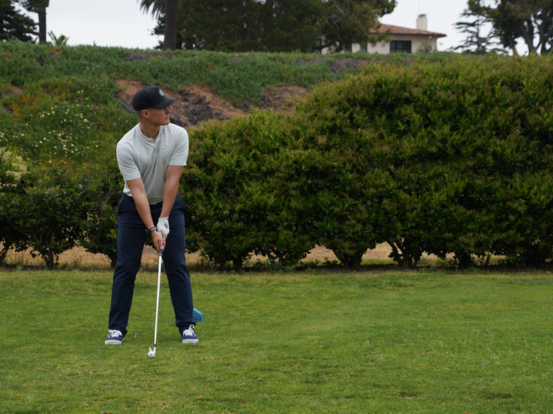 a man holding a golf club on top of a green field