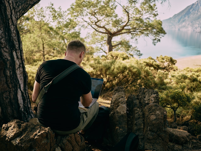 Alone man checking something in laptop while sitting on the rock in the forest