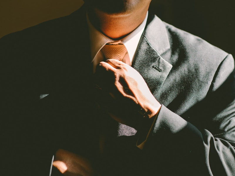 A man in a black suit loosening his tie