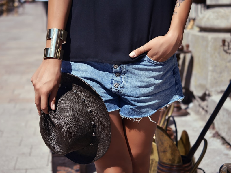 person wearing blue denim short shorts and holding black trilby hat