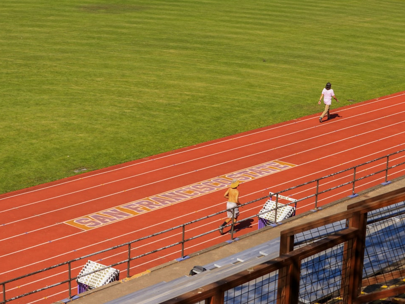 a man walking across a track next to a lush green field