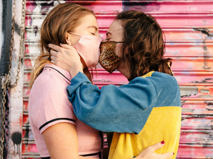 girl in blue and yellow hoodie kissing woman in white shirt