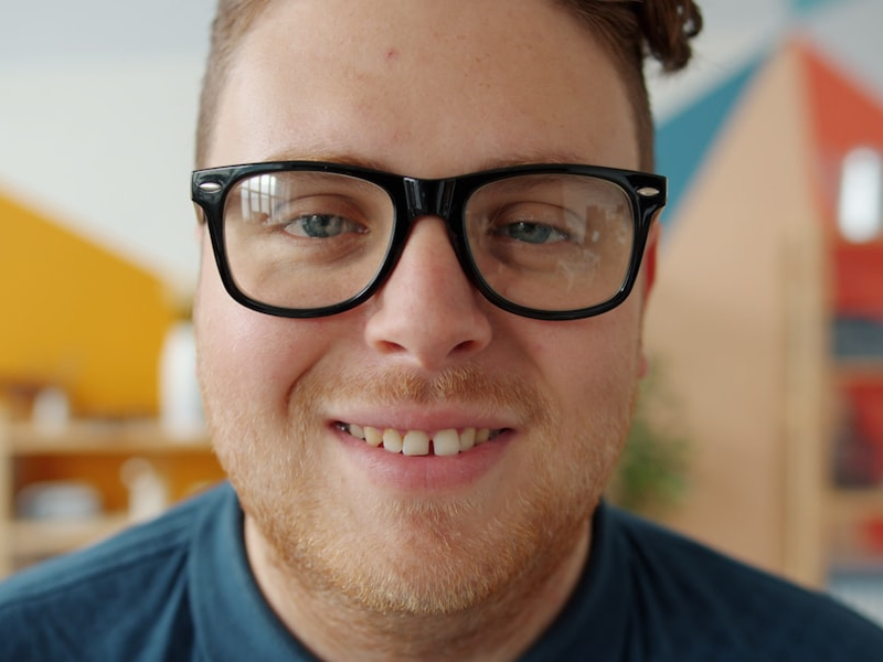 portrait of attractive young man in trendy glasses smiling laughing looking at camera indoors in apartment. Emotions, youth and stylish people concept.