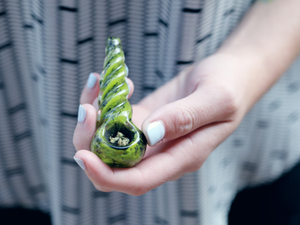 Woman holding a glass cannabis pipe filled with medical grade marijuana.