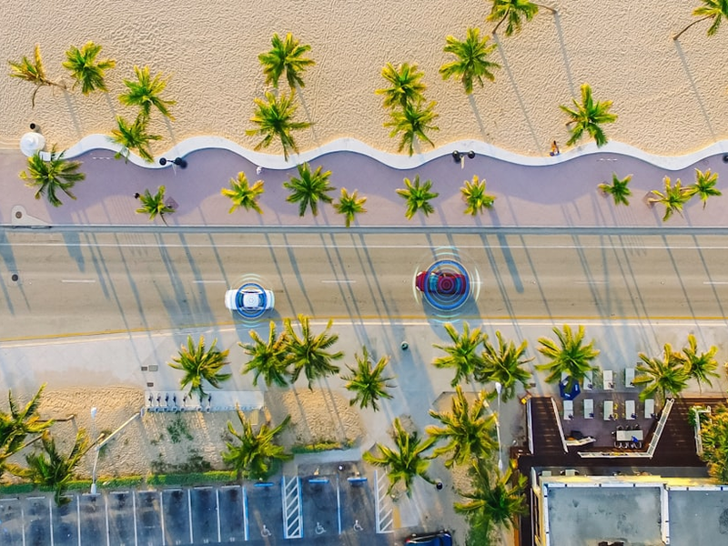 Aerial Drone View: White Autonomous Self Driving Car Moving Through City. Concept: Artificial Intelligence Scans Surrounding Environment, Detecting Cars, Avoids Traffic Jams and Drives Safely.