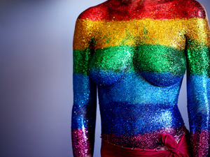 An 18 year old person covered in rainbow body glitter in support of the LGBTQ community and to celebrate gay pride 2018. We used a synthetic cosmetics brush to paint clear hair gel on their torso and then they laid down and I sprinkled the glitter on their body, one stripe at a time. We were able to touch up by dabbing more glitter on after they stood up. We used water-proof adhesive bandages to cover the sensitive areas on the chest and the belly-button.