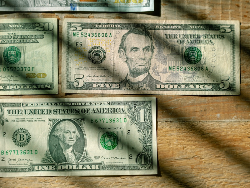 US Currency $100, $20, $5, $1 denominations flat lay on wood background