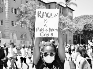 Black woman wearing mask holding protest placard. 