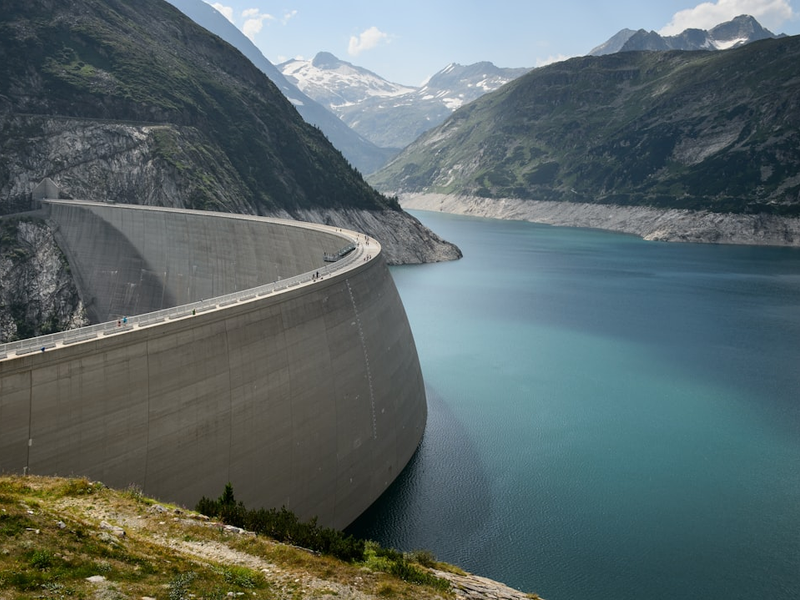 photo of concrete dam in lake near mountains during daytime