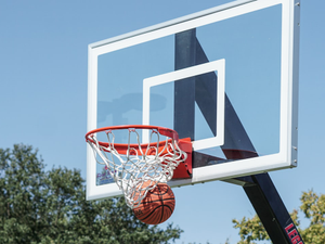 A basket ball going into a basket next to a blue sky with trees in the background.