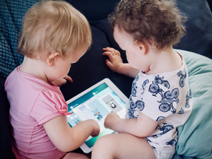 two toddlers sitting on sofa while using tablet computer