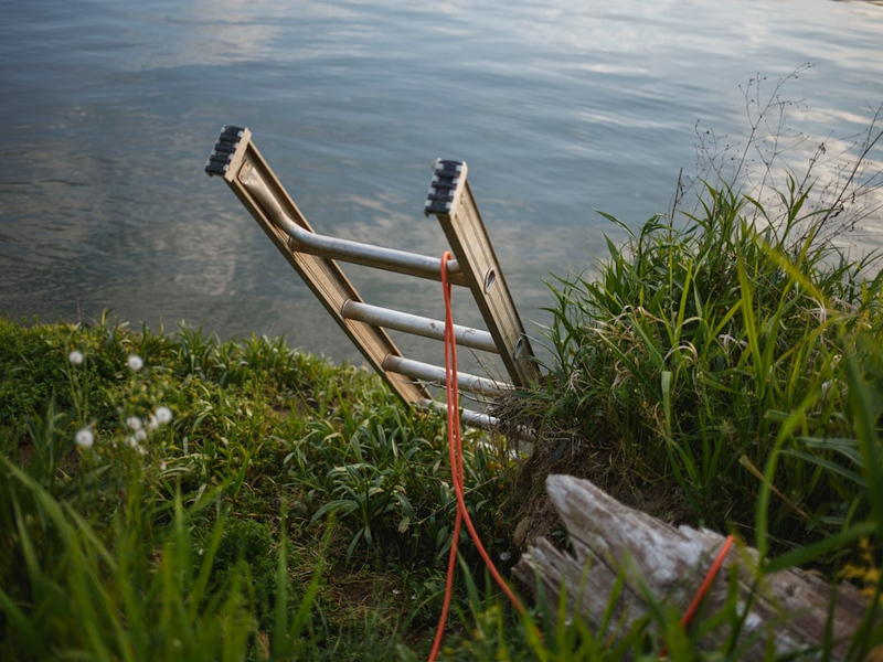 gray metal extension ladder on body of water leaning on soil surface