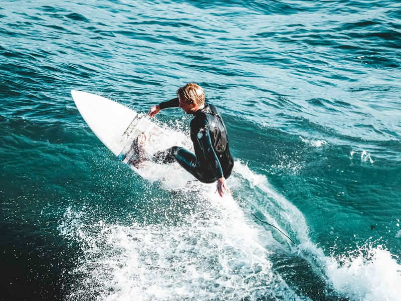 man in black wet suit riding white surfboard on sea waves during daytime