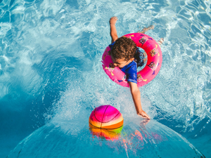 girl in blue tank top and blue shorts holding pink inflatable ring on water