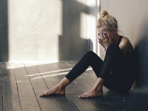 Young teenage girl dancer crying after loss perfomance sits on floor in hall
