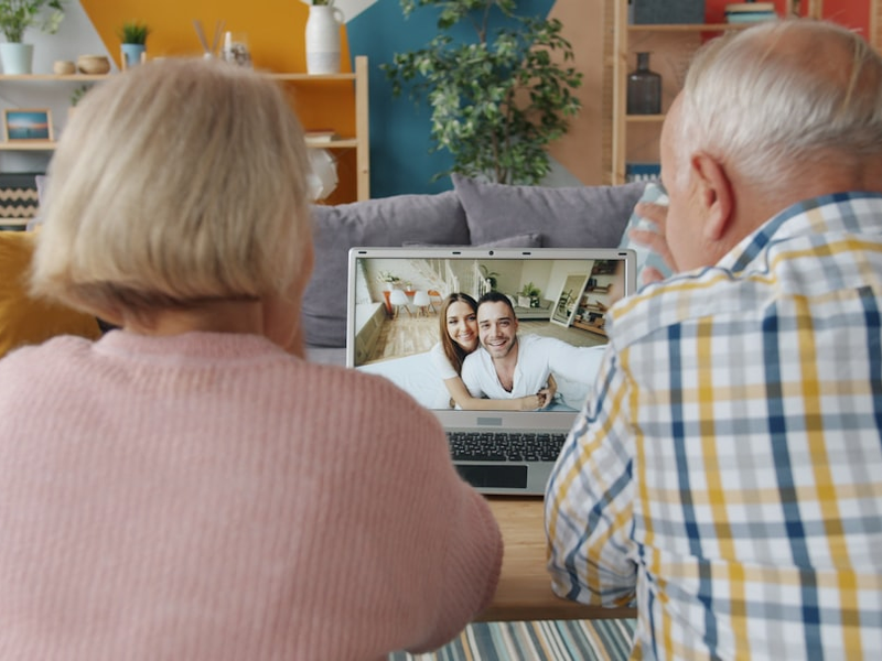 Retired couple is making online video call talking to young people family from home using laptop computer. Modern technology and communication concept.