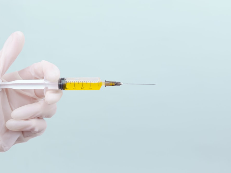 The doctor's hand in a white medical glove holds a syringe with a yellow medicine on a blue background. The medicine. Place for an inscription. Vaccine. Covid 19. Coronavirus.