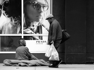 grayscale photo of man with shop bags walking past beggar siting on sidewalk