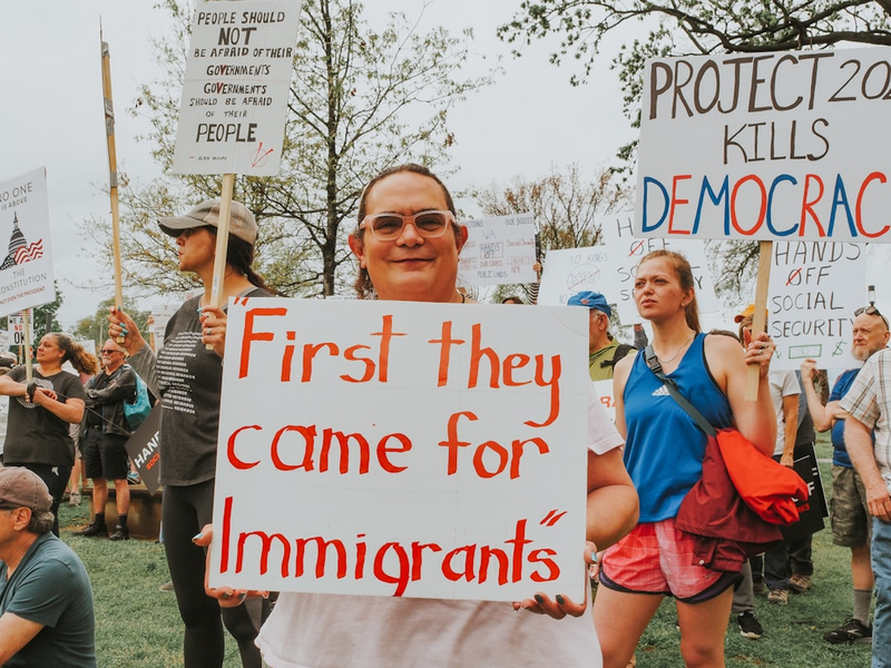 Protesters hold signs about immigrants and democracy.