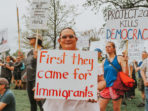 Protesters hold signs about immigrants and democracy.