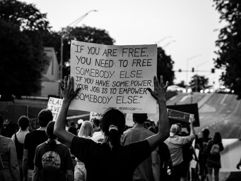 black lives matter protest, with a person holding a sign that says "If you are free, you need to free somebody else. If you have some power, your job is to empower somebody else."