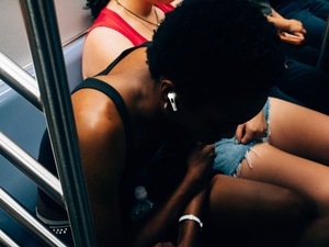 Landscape picture of a black woman enjoying music through her Apple Airpods Pro on a subway in New York, United States. Picture taken with the Fujifilm X100V