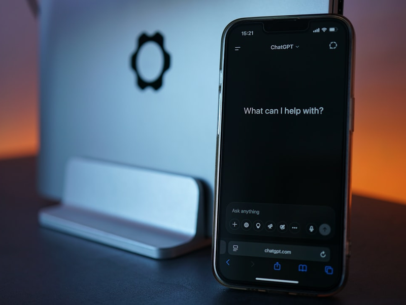 Phone displays chatgpt, next to laptop.