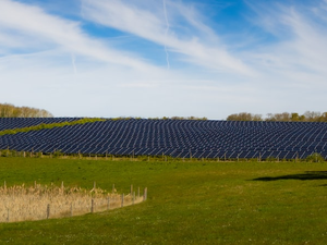 A vast solar farm stretches across a green field under a bright blue sky with wispy clouds, symbolizing clean energy and sustainability.