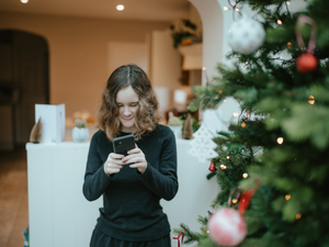 a woman standing in front of a christmas tree looking at her cell phone