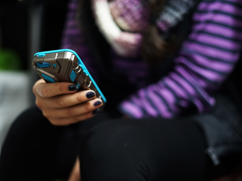 woman in purple and black stripe long sleeve shirt holding blue smartphone
