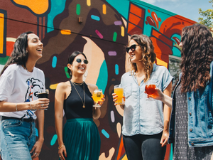 four women holding drinks while laughing together during daytime