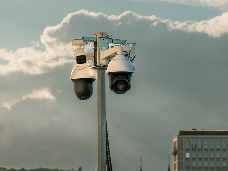 Surveillance Cameras Urban Security Pole City Background. Set of modern CCTV cameras mounted on a metal pole against a cloudy sky in an urban environment. Public safety technology used for monitoring streets and traffic in city areas