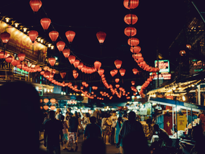people walking between food stalls under chinese lanterns