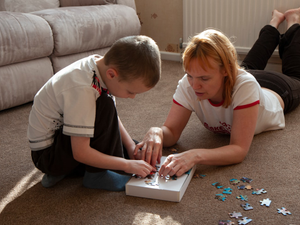 Young boy assembling a colourful jigsaw puzzle on the carpet with his mother at home