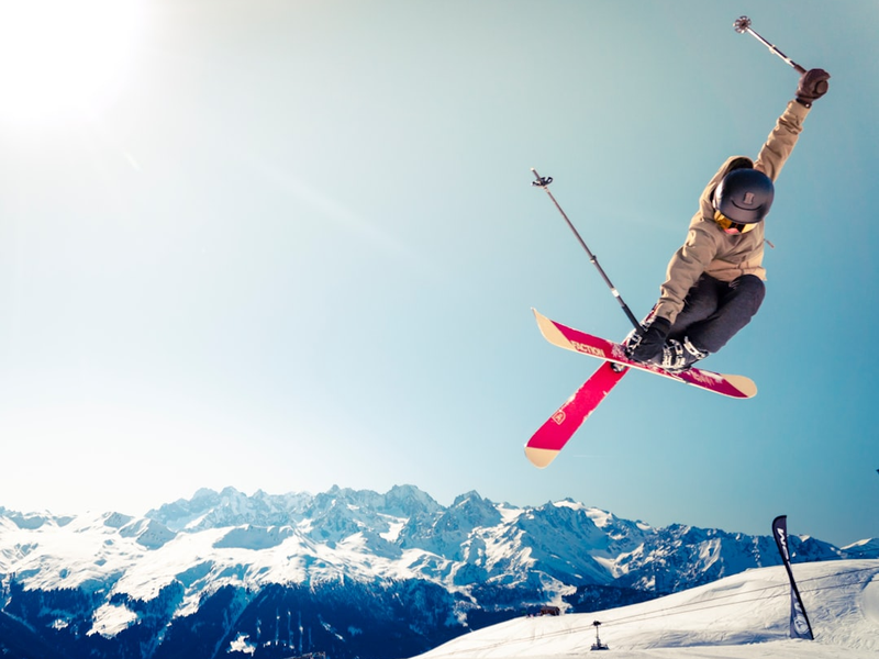 person in brown jacket doing snow ski blade trick