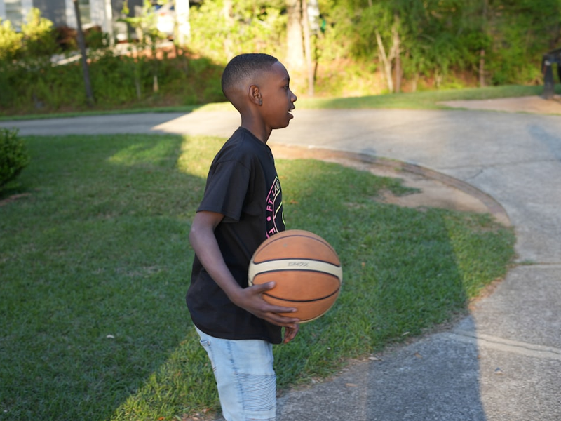 a young boy holding a basketball on a street